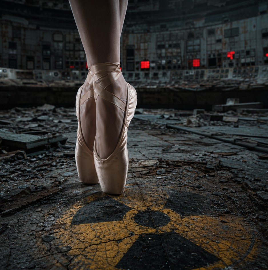 Bailarina en puntas sobre suelo agrietado con símbolo radiactivo en una sala abandonada.